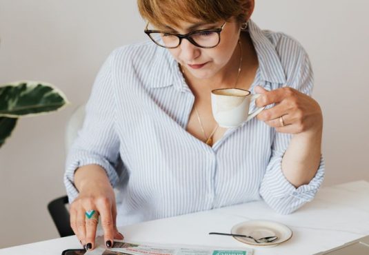 A woman reading stock market articles while drinking coffee at a table.